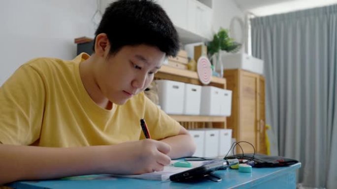 亚洲男孩在家学习在线课程时做作业，社交疏远生活方式理念。