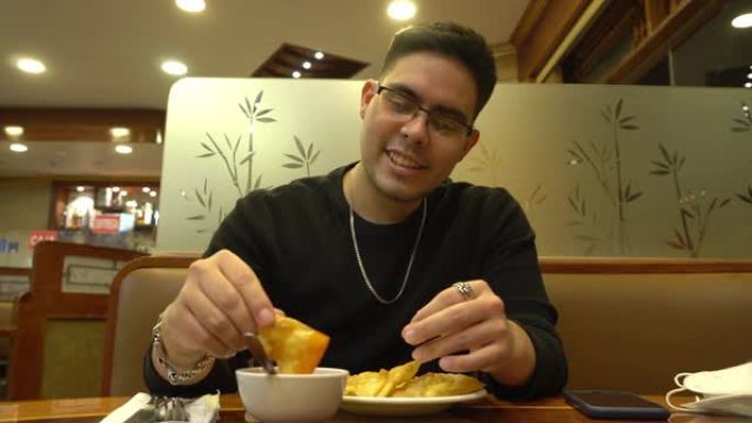 一个戴着眼镜的年轻人用手吃着带有红色罗望子酱的中国菜wantan Chifa，说话和微笑