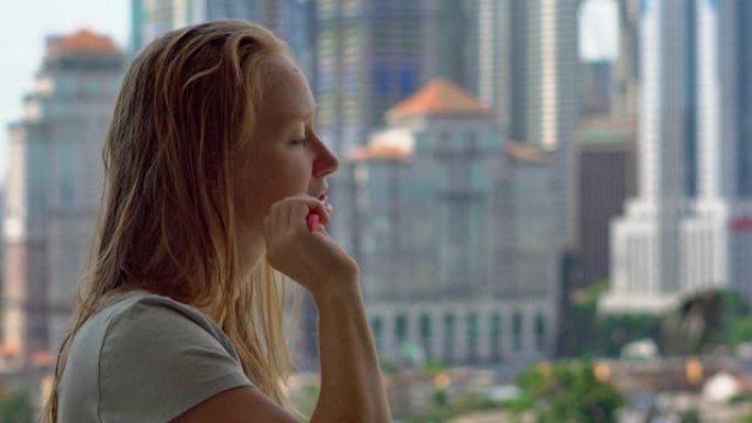 年轻女子站在阳台上刷牙，可以看到充满摩天大楼的市中心
