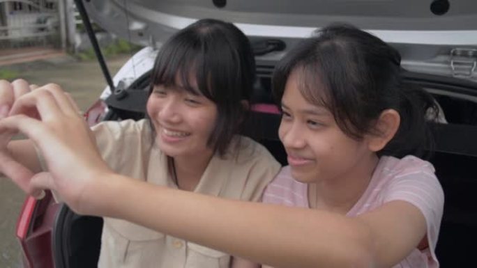 两个亚洲可爱的女性青少年坐在掀背车的后侧，喜欢一起做手势心形。年轻的生活方式。