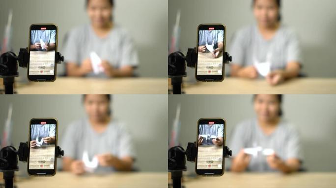 亚洲妇女，年轻的成年人在家里的智能手机上在线制作纸鸟折纸拍打鸟。冠状病毒封锁检疫期间新的正常生活方式