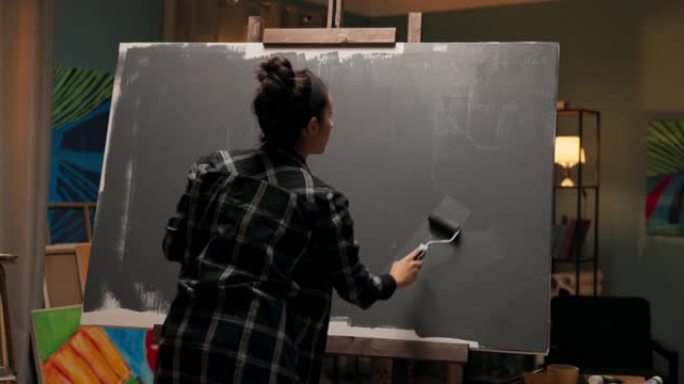 艺术家为绘画准备画布，放入灰色底漆，用一个小滚筒将其从托盘中sc起，她将用它来绘画细节，难以到达的地
