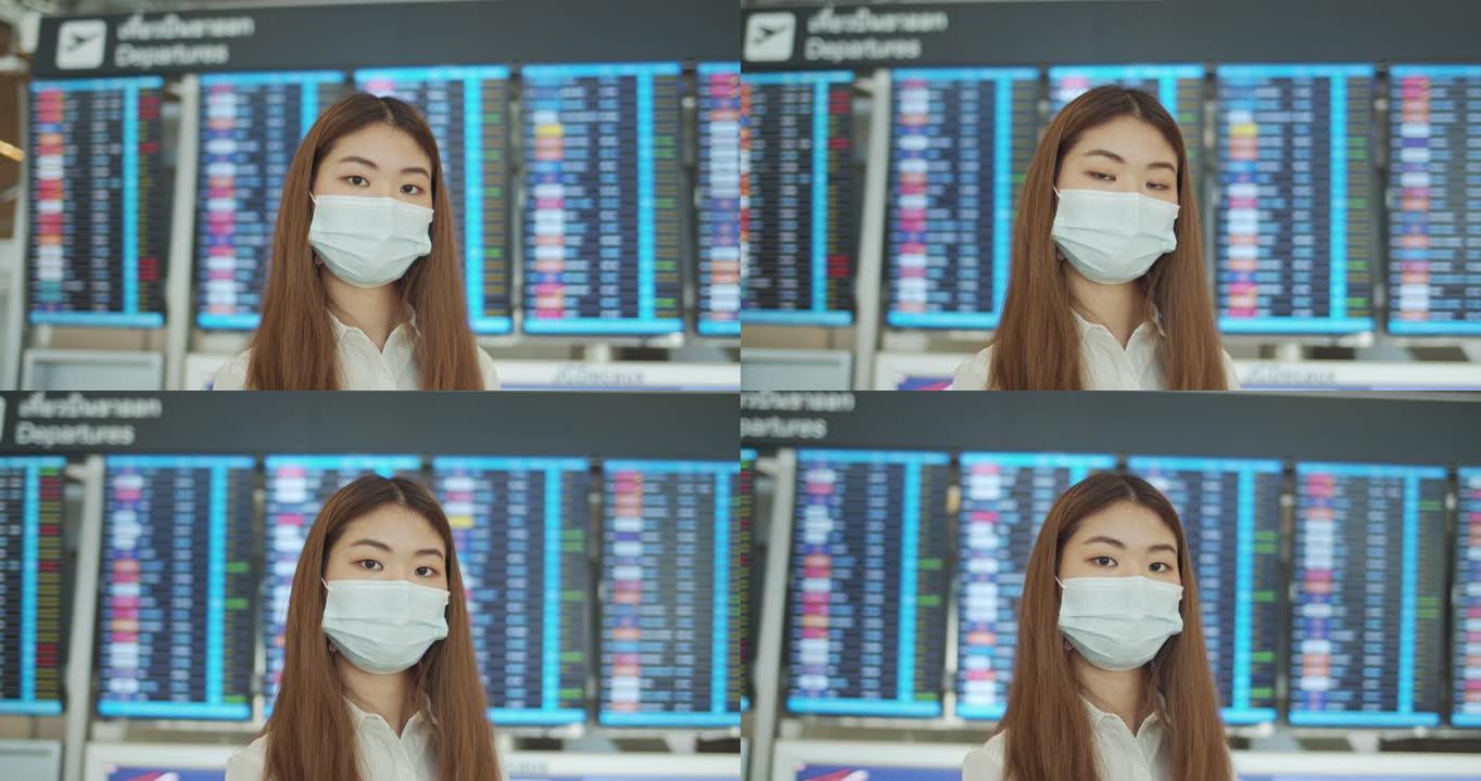 年轻的亚洲妇女站在机场出发板前戴着口罩看相机