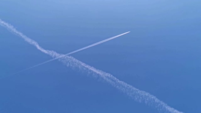 在蓝天上对角线飞行的商用飞机进入框架。飞机航空机场将云雾笼罩。白色客机在蓝天中拉动白色凝结尾迹时运送