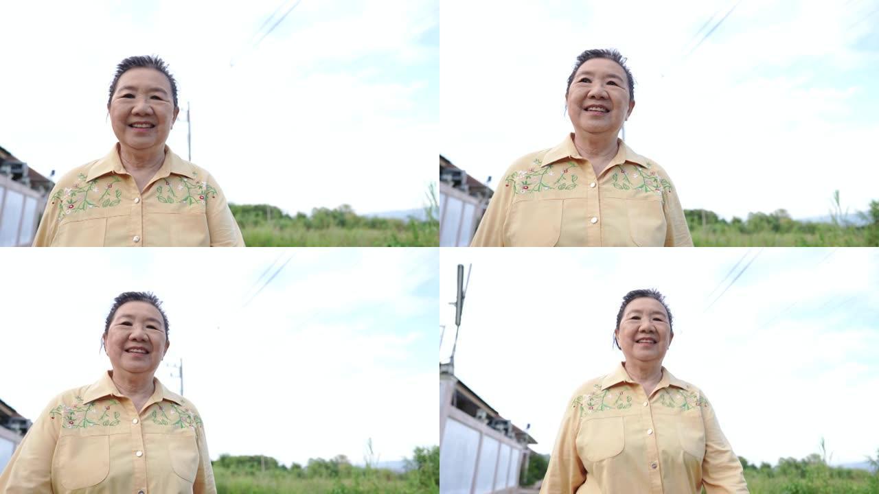 自信的东亚成熟女人看着相机走路，露齿的微笑打手势，在乡村街道上放松运动，女性老人在晴朗的白茫茫的天气
