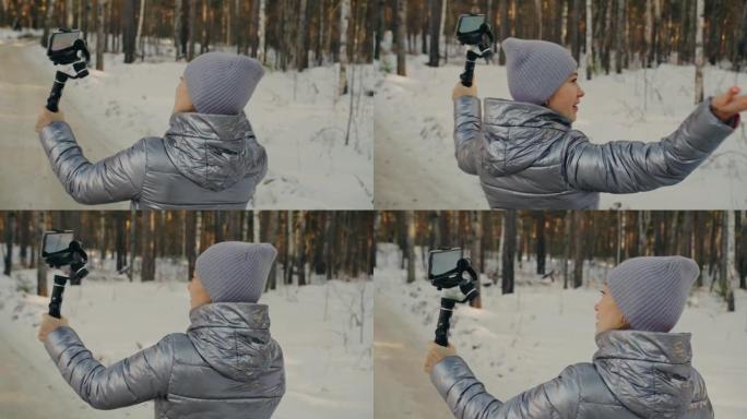 冬季手持薄膜三轴万向节稳定装置的女人为智能手机。摄像师操作员拍摄照片视频。