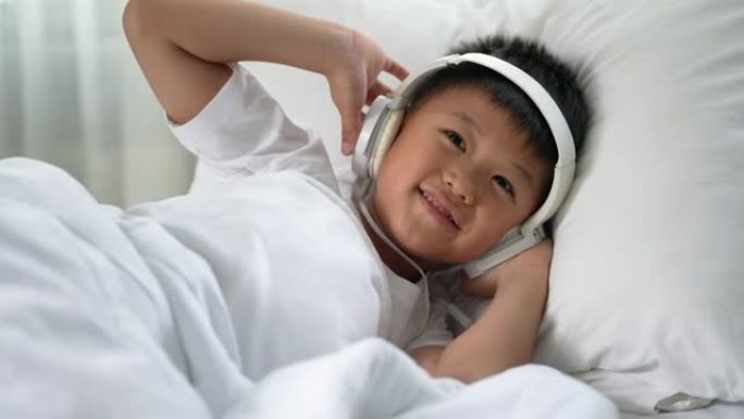 亚洲男孩在白色床上用耳机听音乐