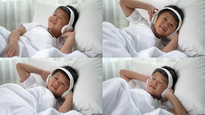 亚洲男孩在白色床上用耳机听音乐
