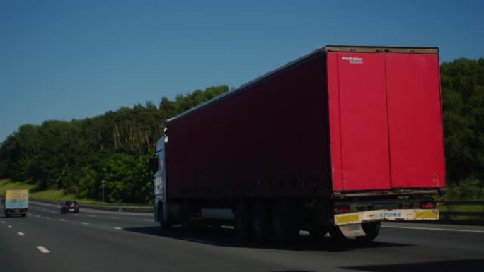 带货运拖车的半卡车驶过高速公路。卡车是白色的，货物拖车是红色的。在黑魔法袖珍电影摄像机6K上拍摄