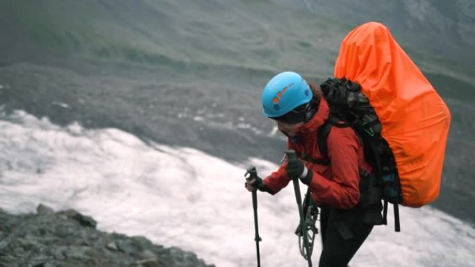 山上的一名妇女带着一个装有装备和登山杖的大背包爬上去