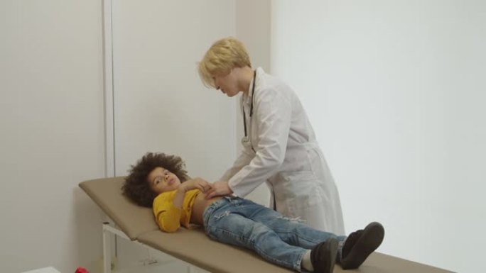 护理女儿科医生在医疗办公室检查患病的学龄前多种族男孩的腹部