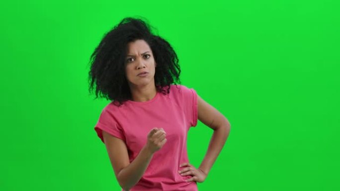 年轻女性非洲裔美国人的肖像发誓，用食指恶毒地摇晃。卷发的黑人妇女在工作室的绿色屏幕上摆姿势。特写。慢