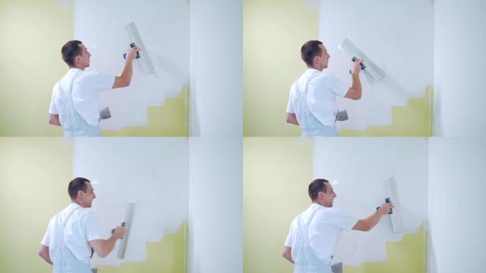 经验丰富的修理工正在抹灰墙壁，使用刮刀，油灰刀和白色现代砂浆，粉刷