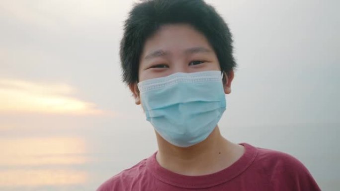 快乐的亚洲男孩戴着口罩，看着华欣海滩的景色，日出背景，生活方式理念。