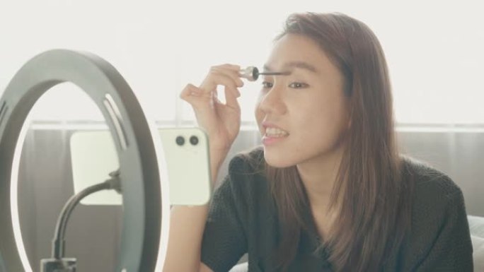 东南亚女人博主广播展示如何化妆和使用化妆品。在镜头前在家录制vlog视频直播。社交媒体概念上的商业在