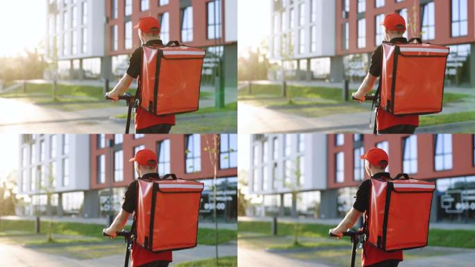 交付男性包裹递送服务人员骑着电动滑板车在日落时带着红色背包在街上的空人行道上。无法识别的年轻快递员骑