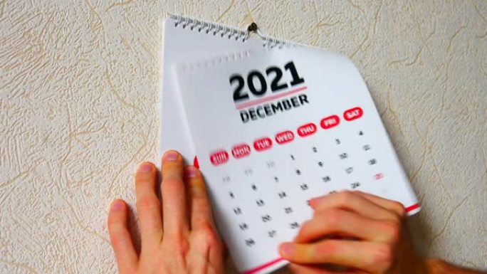 一个男人的手的特写镜头撕下墙上2021日历的12月页，然后是新2022日历的标题页