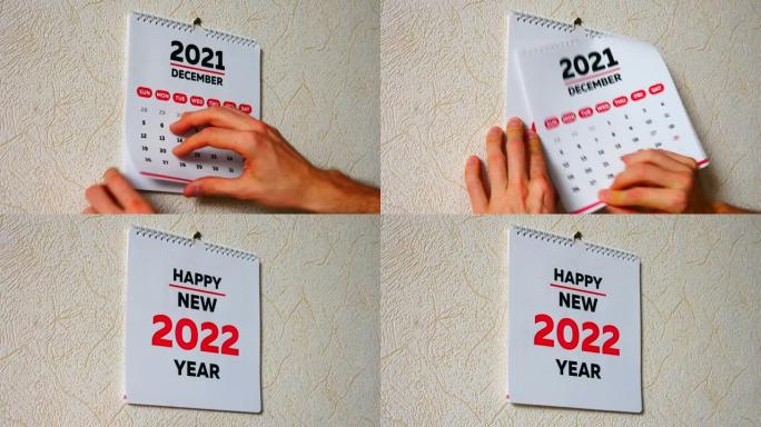一个男人的手的特写镜头撕下墙上2021日历的12月页，然后是新2022日历的标题页