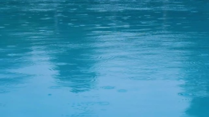 雨滴在光滑的蓝色水面上形成的池塘涟漪