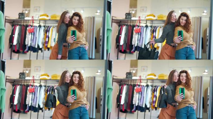 在一家购物中心的服装店里，两个时尚的女孩在镜子前用智能手机或手机自拍。