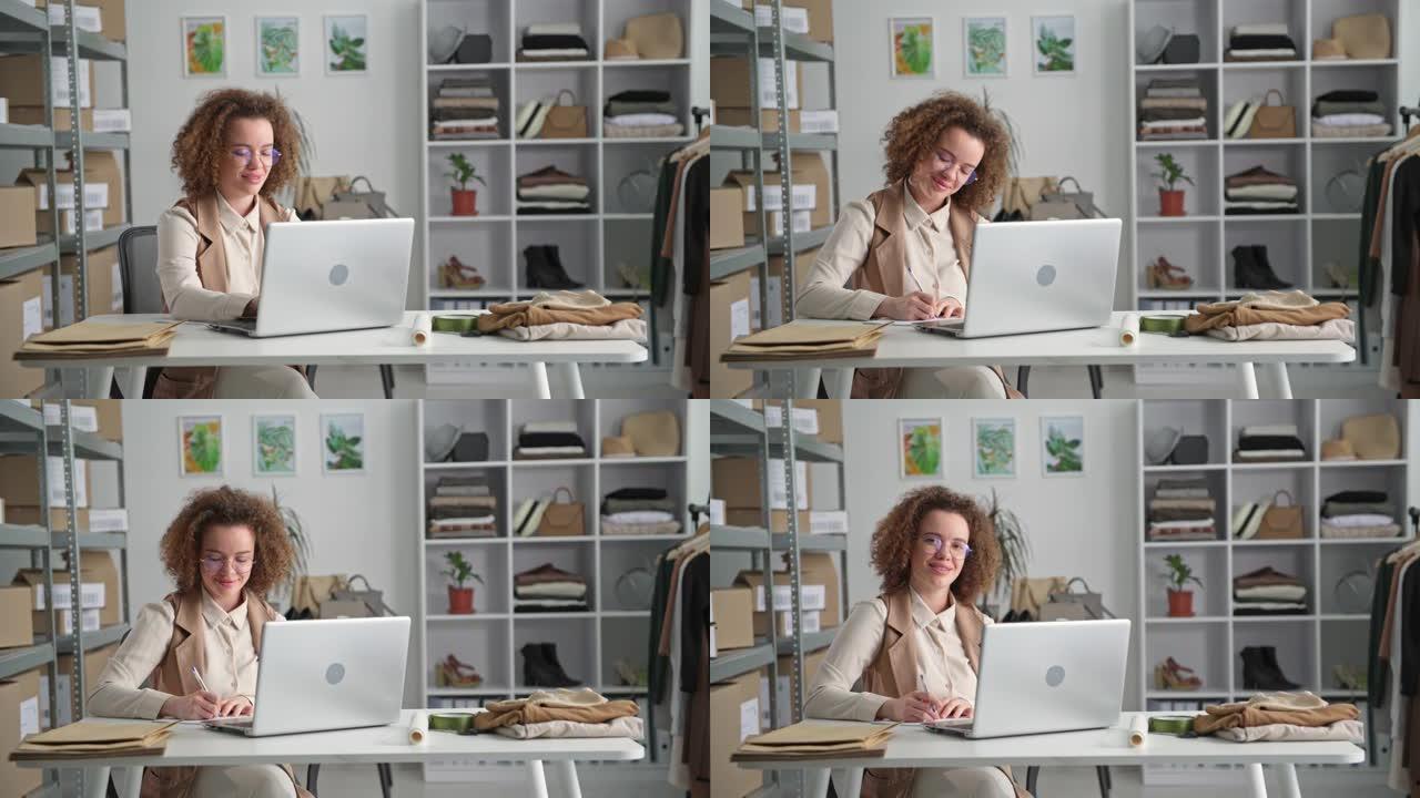 小型企业，一位年轻女子坐在服装店的桌子旁时在笔记本电脑上在线下订单的肖像