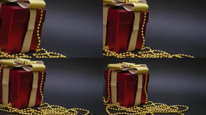 黑色背景上带有金丝带和金色珠子的红色礼品盒。
