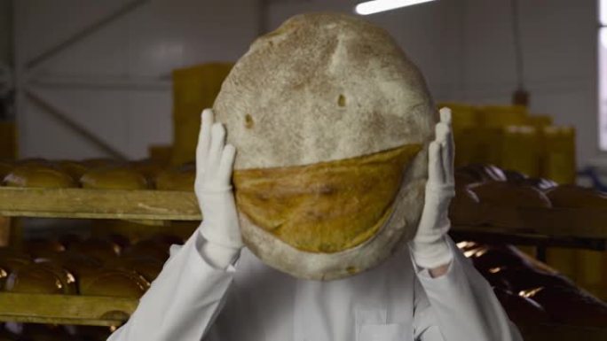 穿着制服的面包师举起了一条大面包，脸上露出微笑的表情