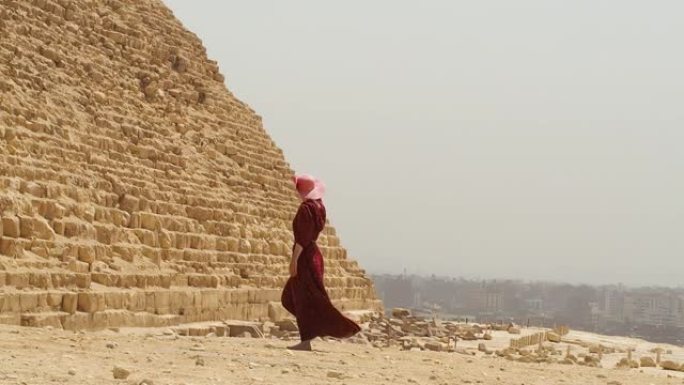 一个穿着长裙的女人在吉萨金字塔旁边经过