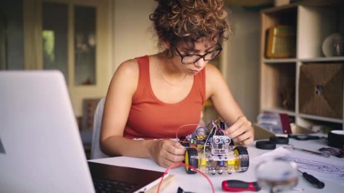 女机器人工程师，在她的创意家庭工作室中，将自动自动驾驶机器人汽车的电缆与带有主板via的传感器连接起