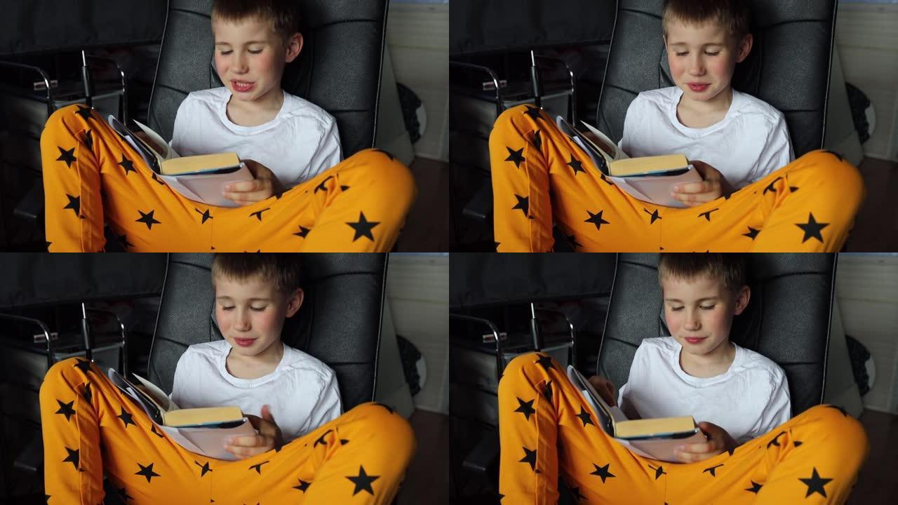 坐在家里椅子上的男生的特写镜头。男孩大声朗读纸质书，翻页，在家学习