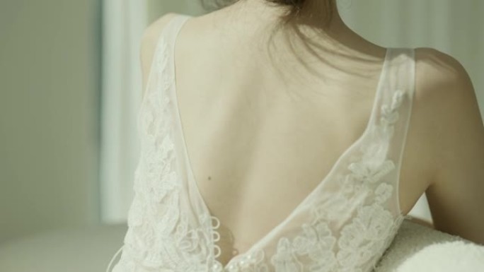 穿着白色连衣裙的美丽亚洲新娘坐在落式窗前的沙发上，以慢动作拍摄