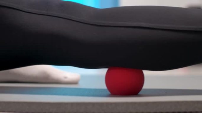 运动苗条的白人女性在室内用按摩球在健身垫上自我按摩大腿。自我隔离按摩