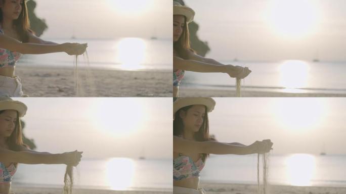 慢动作拍摄了一个剪影年轻美丽的亚洲女人，用手握着沙子对着光线，阳光在清澈的海水上反射，落在人掌心上的