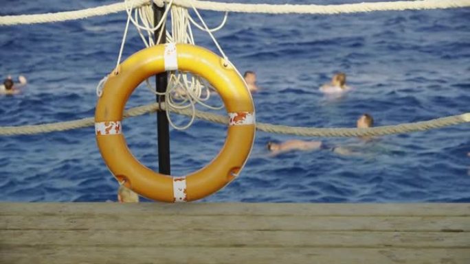 救生圈悬挂在人们游泳的大海背景下。愿意营救溺水的游泳者。