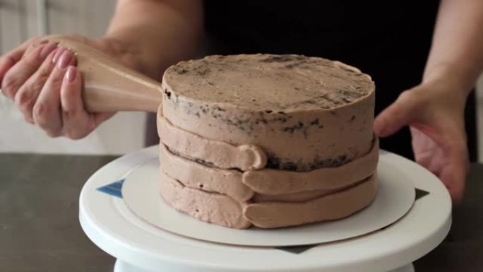 4k女糕点厨师将巧克力奶油应用于带有糕点袋的巧克力海绵蛋糕，特写镜头。慢动作。蛋糕制作过程。