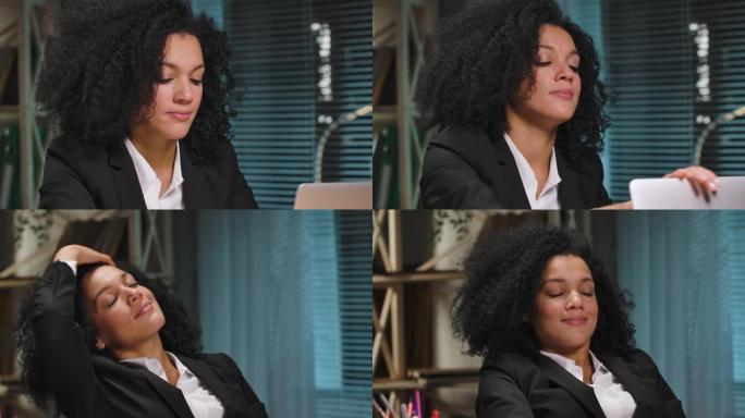 非裔美国妇女的肖像完成工作，关闭笔记本电脑，闭上眼睛放松。女商人在工作场所摆姿势，坐在办公室的桌子旁