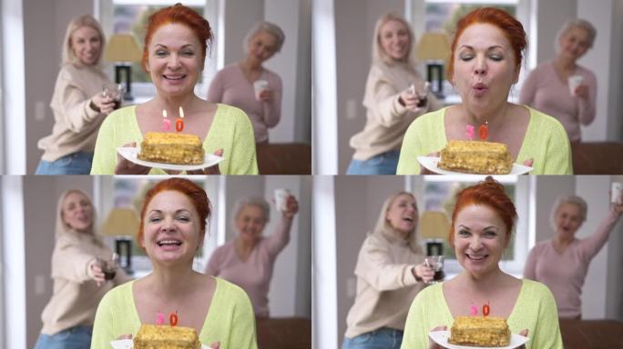 前视图快乐的女人在蛋糕上吹蜡烛，许愿看着相机微笑。兴奋的美丽白人女士的肖像在家里与朋友合影庆祝50岁