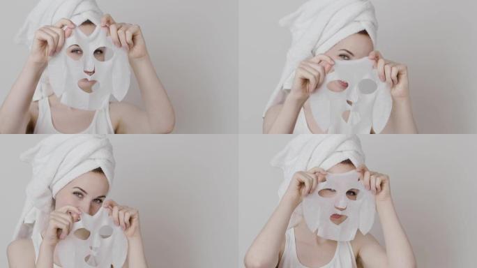 头上戴着毛巾的年轻女子，脸前拿着化妆品面膜