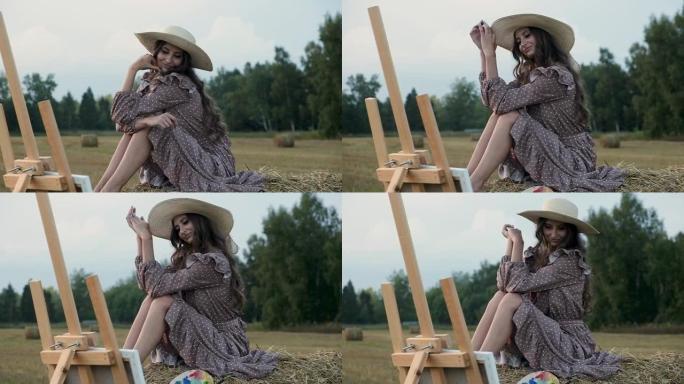 穿着太阳裙和帽子的幸福女人坐在干草堆上，看着彩绘的照片