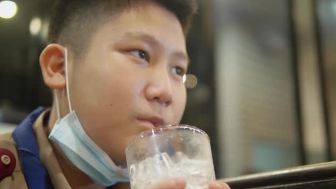 快乐的亚洲童子军制服在美食广场享受他的饮料，生活方式理念。