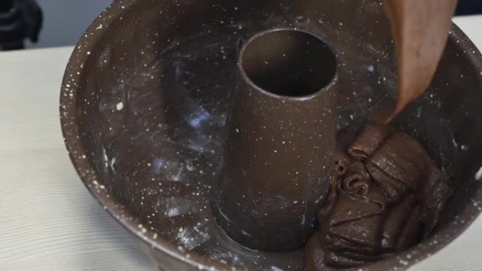 糕点厨师将棕色面团放入圆形巧克力口味蛋糕的烤盘中的特写镜头。