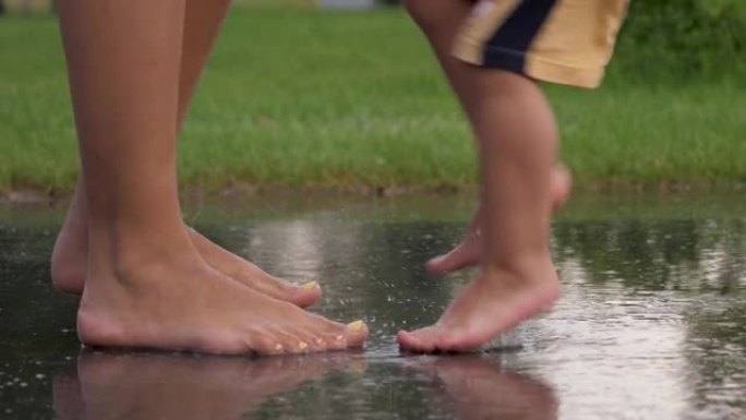 嬉戏的婴儿和母亲的腿赤脚踩在沥青上的水坑上