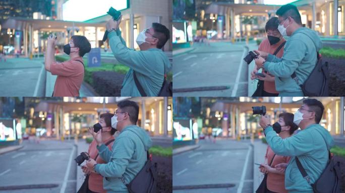 亚洲中国中年夫妇游客晚上在繁忙的吉隆坡城市街道用相机拍照，霓虹灯带面罩