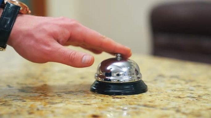 接待处的酒店钟声。男人的手按下铃铛按钮打电话给酒店的接待员。客户触摸金属报警器。特写。