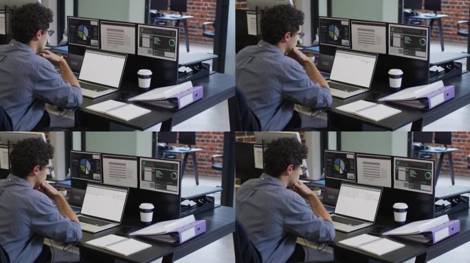 白人男子坐在办公桌前观看笔记本电脑和计算机屏幕上的编码数据处理