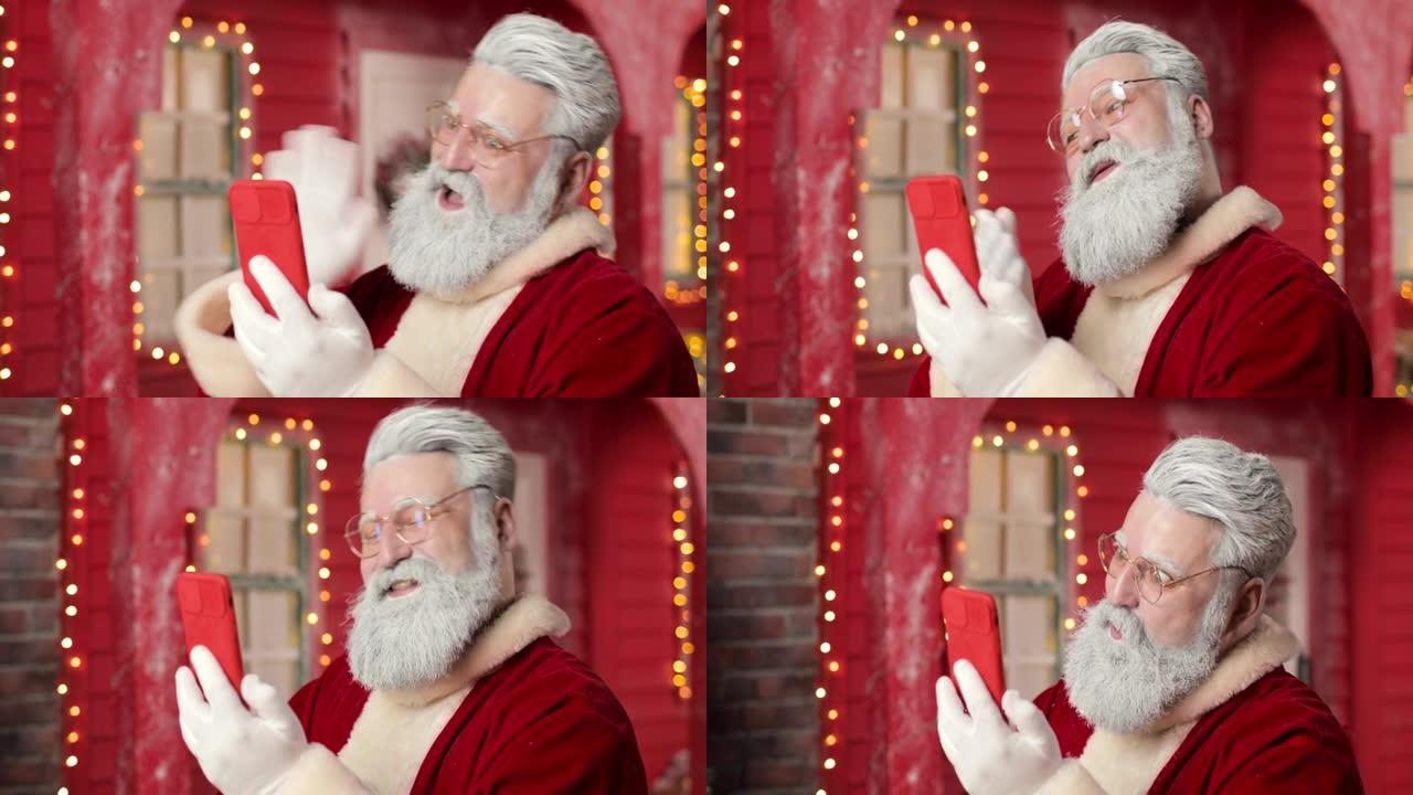 圣诞老人的特写镜头，微笑并通过视频链接与使用智能手机的人交流，背景是一个美丽的新年装饰工作室中的红房