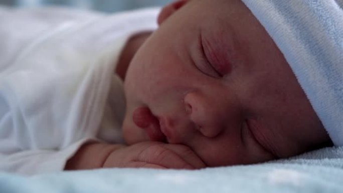 初生婴儿脸部肖像的特写镜头早期在蓝星背景下睡觉。孩子在帽子上生命的开始。婴儿，分娩，出生的最初时刻，