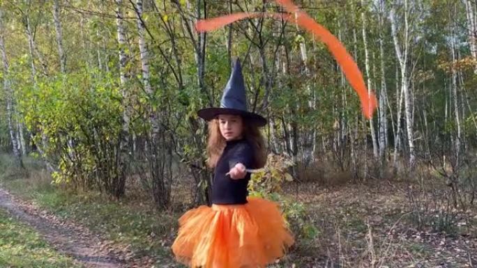 拿着魔杖的小女孩女巫站在森林小路上。万圣节概念。