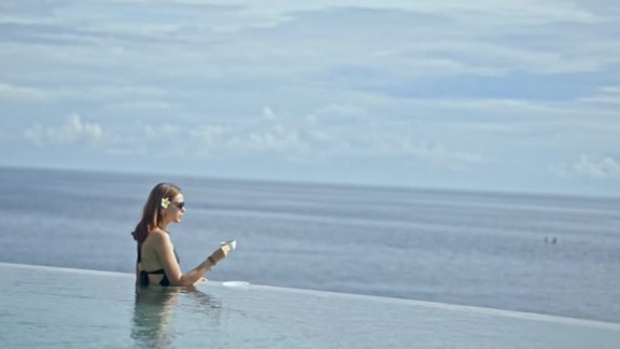 女人在巴厘岛度假村的游泳池度假时从杯子里喝茶。概念无限，地平线，涟漪