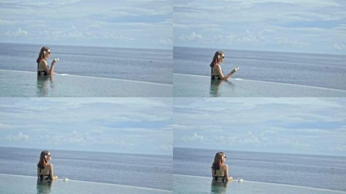 女人在巴厘岛度假村的游泳池度假时从杯子里喝茶。概念无限，地平线，涟漪